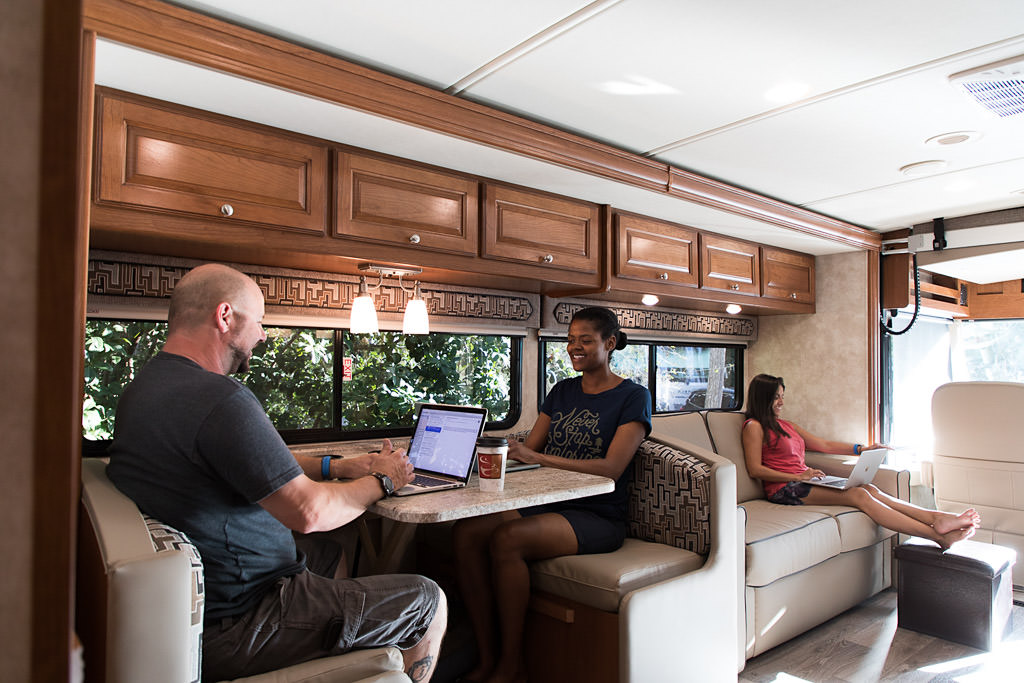 Kenny and Sabrina at the dinette, and Nadia on the couch all working on their laptops.