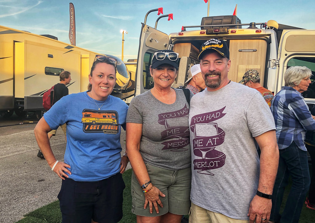 Three people posing outside motorhomes in the display.