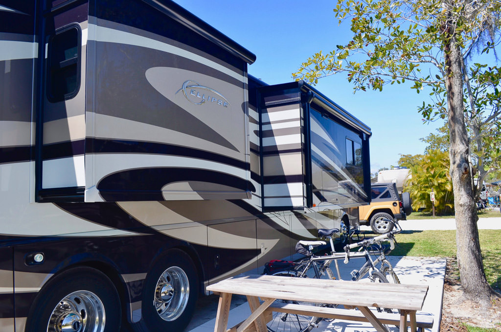 Bikes and a picnic table next to a parked Winnebago Ellipse with the slides out.