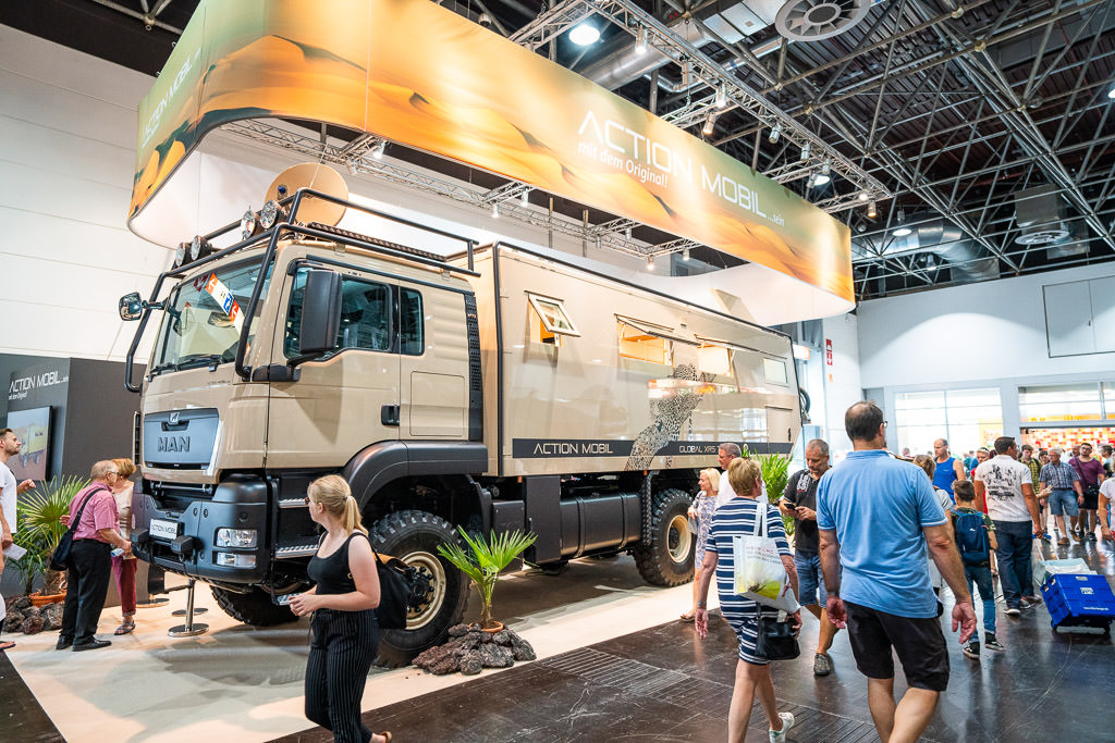 Crowd of people walking past overland vehicle.