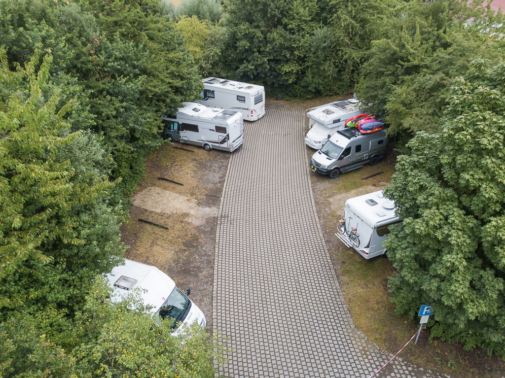 Winnebago Revel parked alongside 5 other motorhomes in small campground surrounded by trees.